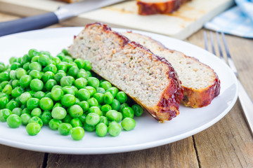 Homemade meatloaf garnished with green peas on a white plate