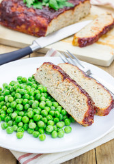Homemade meatloaf garnished with green peas on a white plate