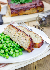 Homemade meatloaf garnished with green peas on a white plate