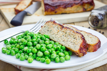Homemade meatloaf garnished with green peas on a white plate