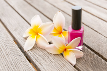 Fuchsia nail polish in the bottle and flowers on the woody background