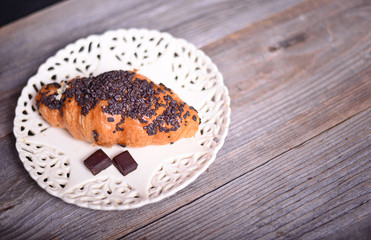Chocolate croissant on white plate on wooden background