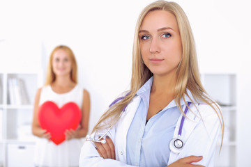 Woman doctor  in  hospital, a large red heart  in patient hand  at the background