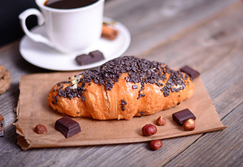 Chocolate croissant with coffee on wooden background