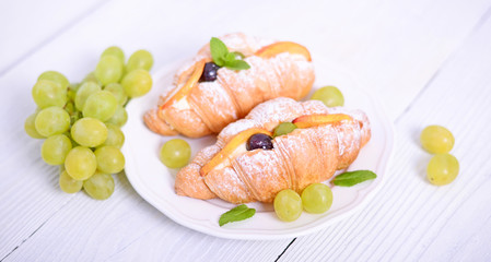 Fresh croissant with grapes on white background