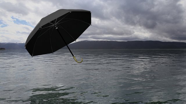 Umbrella floating above water, with distant mountains and cloudy sky on background.