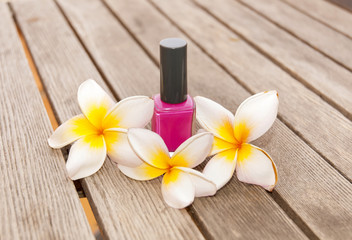 Fuchsia nail polish in the bottle and flowers on the woody background