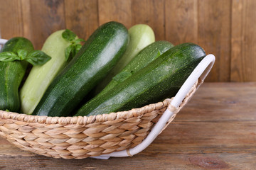 Fresh zucchini with squash and basil in wicker basket on wooden background