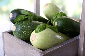 Fresh zucchini with squash and basil in wooden box on bright background