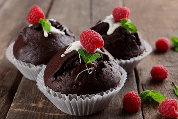 Delicious chocolate cupcakes with berries and fresh mint on wooden table close up