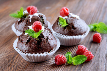 Delicious chocolate cupcakes with berries and fresh mint on wooden table close up