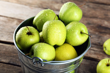 Ripe green apple in metal bucket on wooden table close up