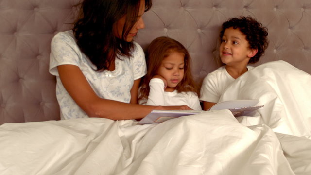 Smiling Hispanic mother with her children in bed