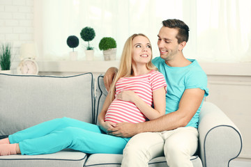 Young pregnant woman with husband on sofa in room