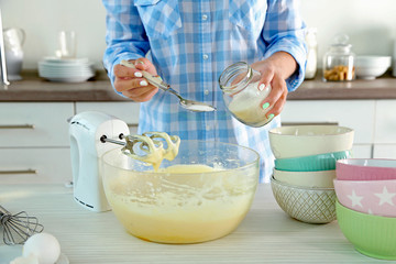 Young woman making rainbow cake in kitchen
