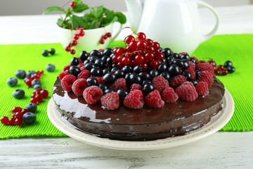 Delicious chocolate cake with summer berries on wooden table with green napkin, closeup