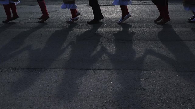 Kolo - people dancing Serbian folk dance, focus on legs and shadows on the pavement