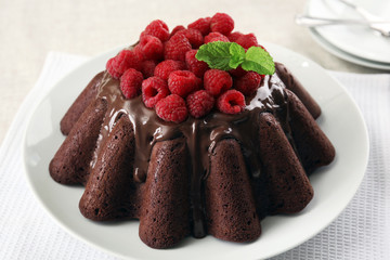 Tasty chocolate muffin with glaze and raspberries on table close up