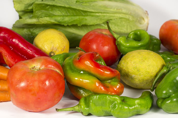 Red and green peppers beside tomatoes, lemons, carrots and a lettuce