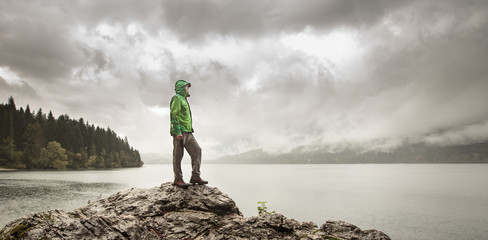 Man standing on a rock beside a mountain lake in rain
