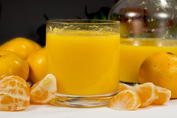 Glass of orange juice beside a glass jar, full tangerines and peeled mandarin segments © Alonso Aguilar