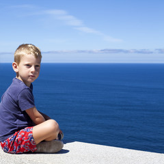 Niño rubio sentado frente al mar