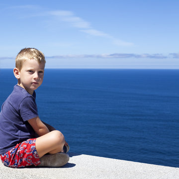 Ni&ntilde;o rubio sentado frente al mar