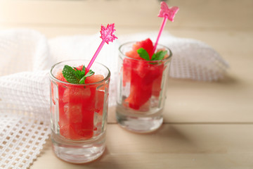 Cold watermelon pieces in glasses, on wooden table background