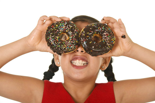 latin child playing with donuts in her hands putting them on her face as cake eyes