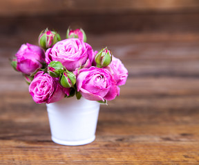 Pink roses in a vase on wooden background
