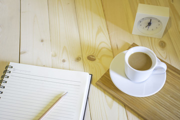 Coffee cup with notebook in the morning sunshine on wood floor.