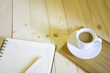 Coffee cup with notebook in the morning sunshine on wood floor.