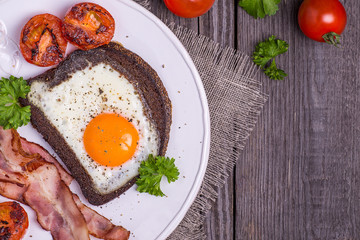Fried eggs in rye bread with bacon, tomatoes and parsley in rust