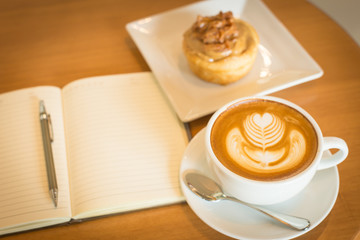 Apple cinnamon roll served with latte art coffee and notebook on