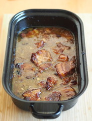 Baked pork belly with a sauce in a black roasting pan on a wooden table. Traditional specialty form the Czech Republic  called 