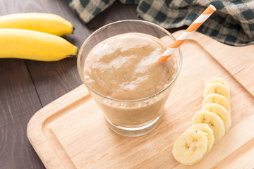 Banana smoothie and fresh banana on wooden background