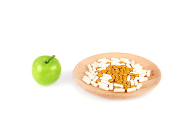 Pills on wooden plate and an apple isolated on white