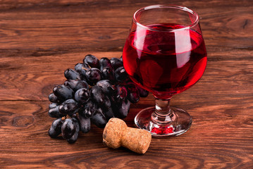 Bunch of fresh grapes, cork and glass of wine on a wooden background