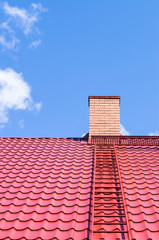 Brick chimney on red roof with metal ladder