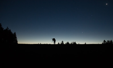 Naklejka na ściany i meble photographer silhouette with tripod standing in the night with stars