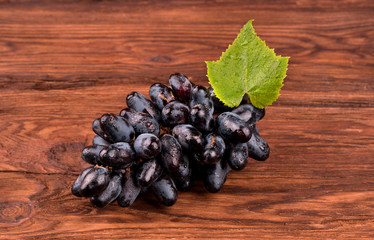 Bunch of fresh grapes with drops and leaf on a wooden background
