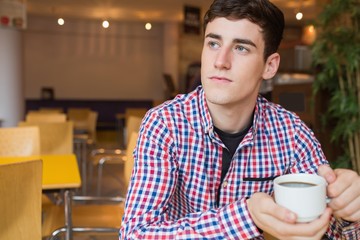 Fototapeta na wymiar Thoughtful young man holding coffee cup