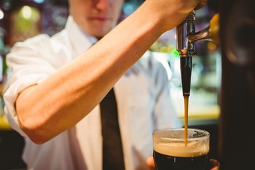 Fototapeta na wymiar Barkeeper holding beer glass below dispenser tap