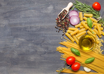 Different pasta, condiment, olive oil and tomatoes on dark woode