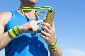 Brazilian athlete with green and yellow wristbands using gold medal mobile phone against blue sky