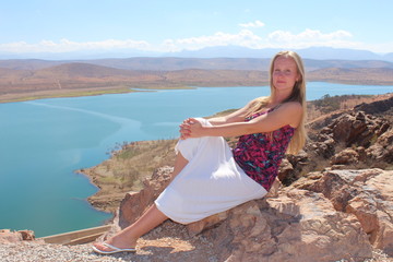 A young woman sit on the rock and look at the camera.

