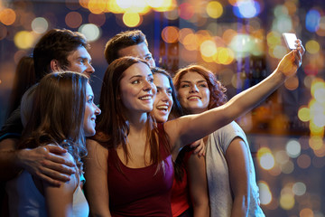friends with smartphone taking selfie in club