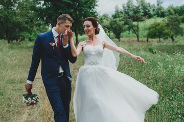 Bride and groom at wedding Day walking Outdoors on spring nature. Bridal couple, Happy Newlywed woman and man embracing in green park. Loving wedding couple outdoor. Bride and groom