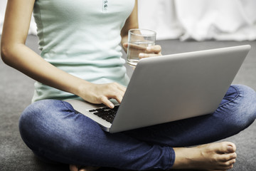 young woman holding a glass of water in a sitting position while using her laptop
