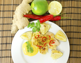 A roasted in the oven chicken breast fillet garnished with chili, ginger, coconut and lime served in a plate with mango sauce, raw vegetables on a white background. A healthy asian cuisine dish.